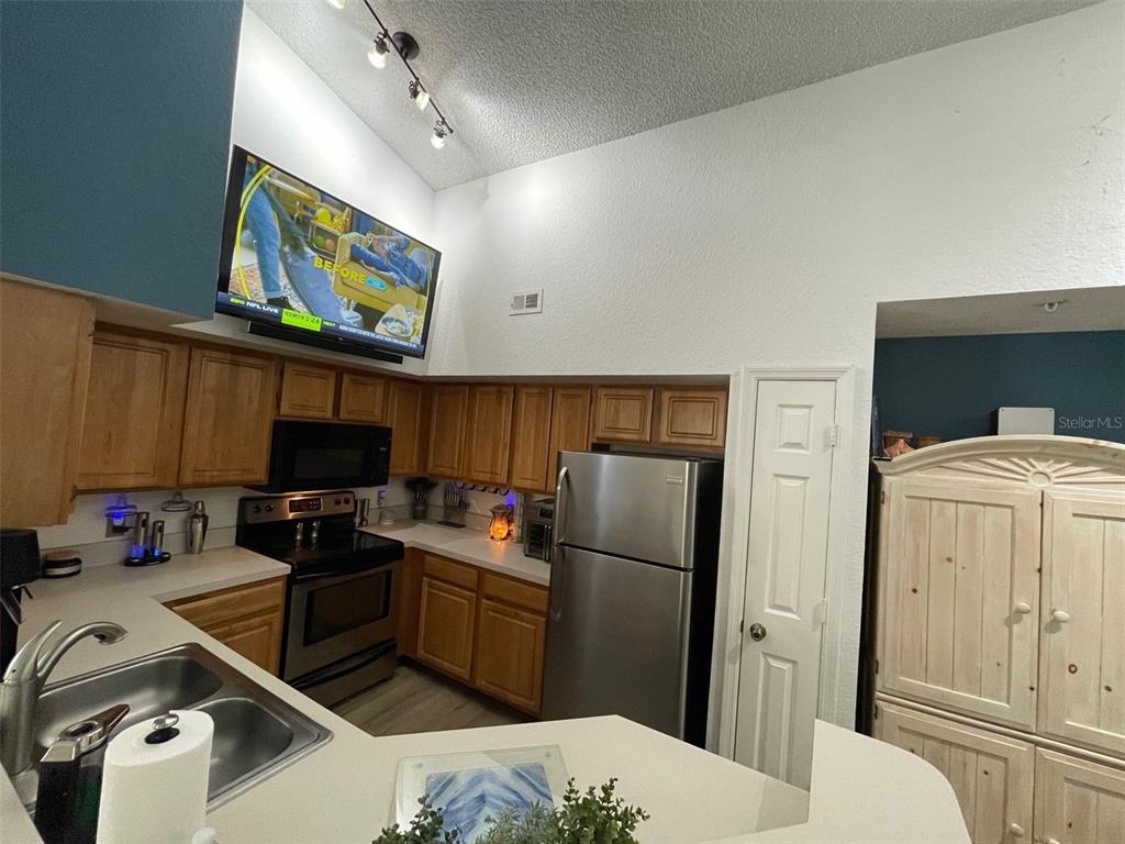 A kitchen features wood cabinets, stainless steel appliances, and a television mounted above the stove — 13103 MULBERRY PARK DRIVE UNIT 831, ORLANDO, FL