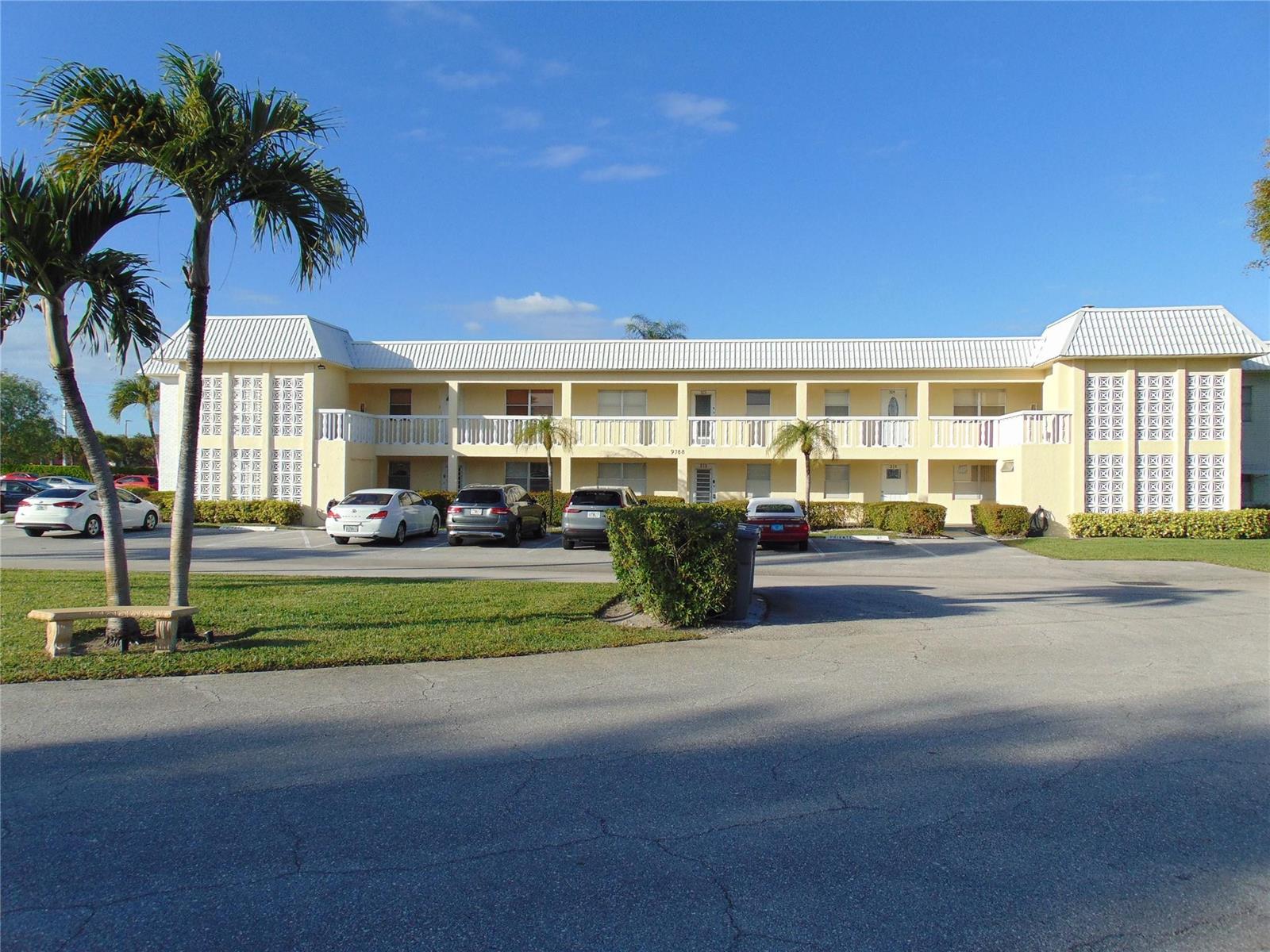 A two-story yellow apartment building with a white roof sits behind a parking lot — 9788 Marina Boulevard # 313, Boca Raton FL 33428, BOCA RATON, FL