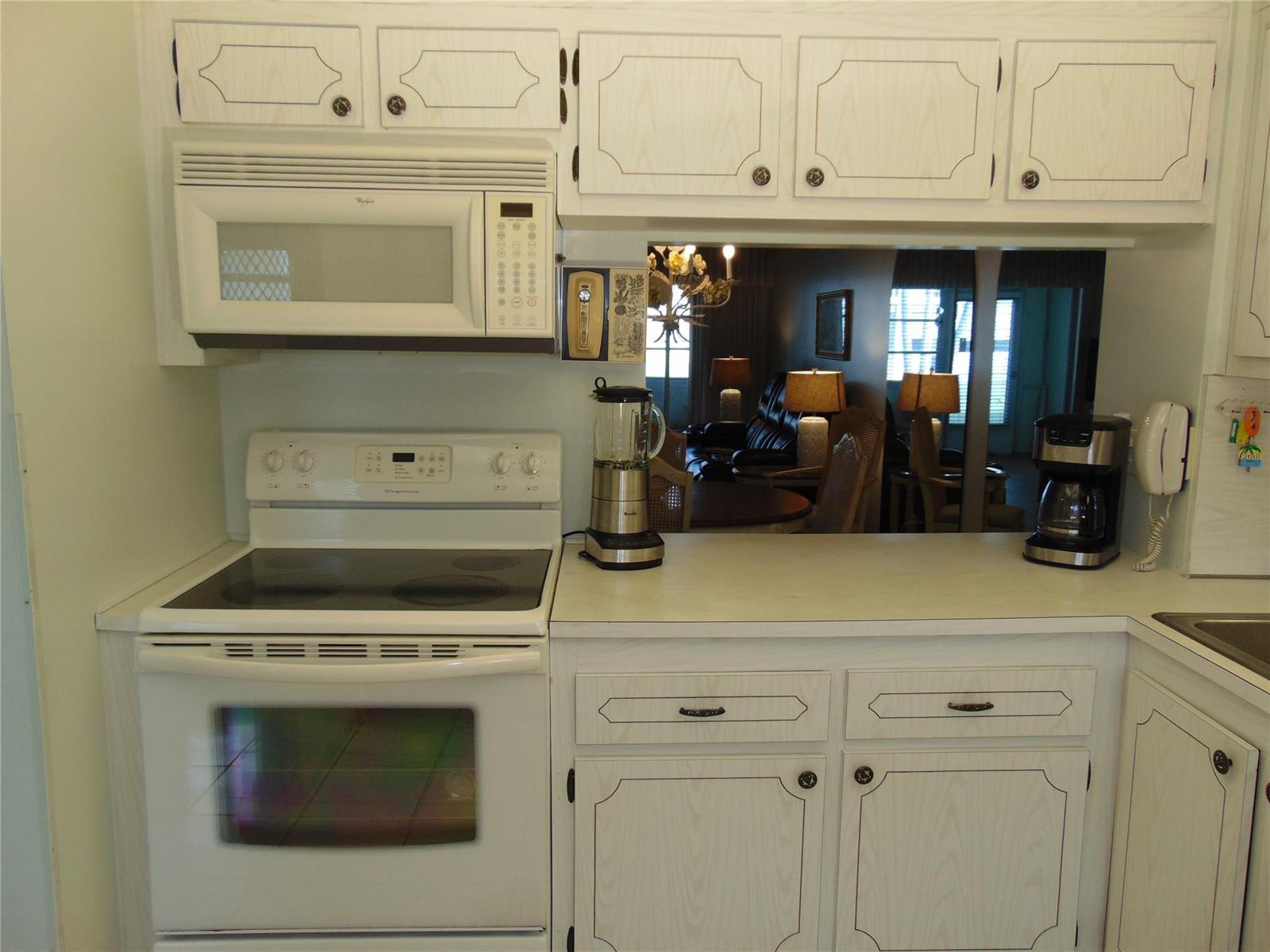 A kitchen features white cabinets, a white electric range, a microwave, and a pass-through window — 9788 Marina Boulevard # 313, Boca Raton FL 33428, BOCA RATON, FL
