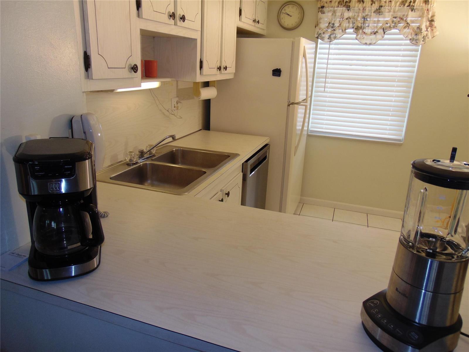 A kitchen features white cabinets, a double sink, a refrigerator, and appliances on the counter — 9788 Marina Boulevard # 313, Boca Raton FL 33428, BOCA RATON, FL