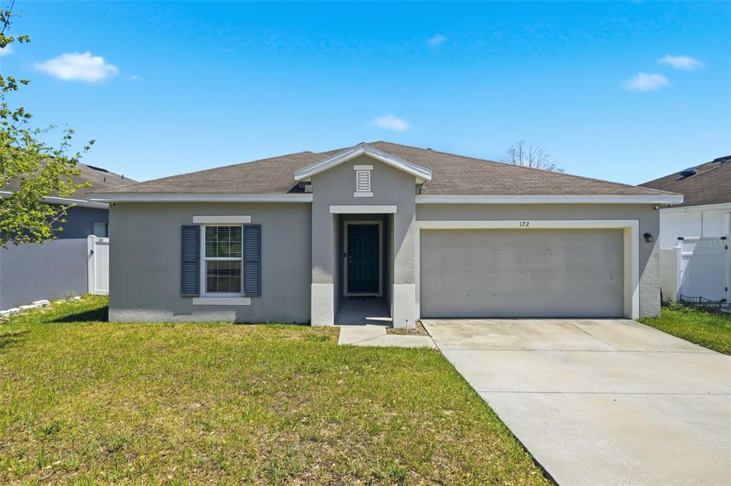 A single-story house with a gray stucco exterior, a two-car garage, and a front lawn — 172 TANAGER STREET, HAINES CITY, FL