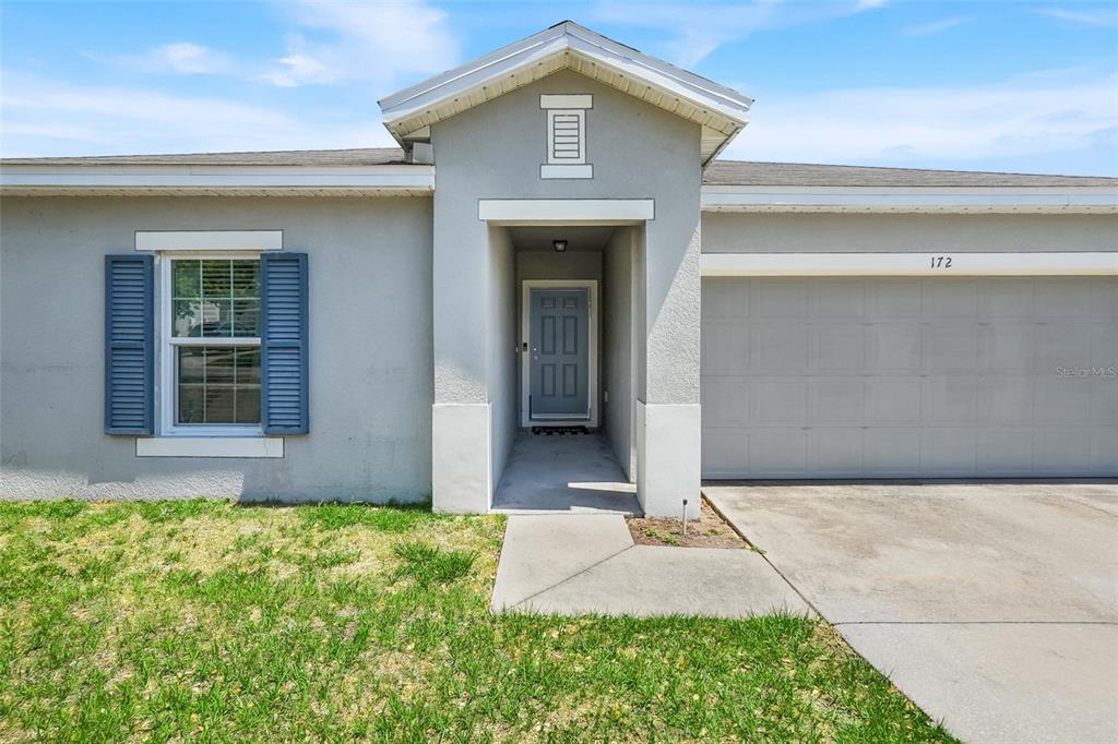 A single-story house exterior features a gray stucco facade, a blue front door, and a garage — 172 TANAGER STREET, HAINES CITY, FL