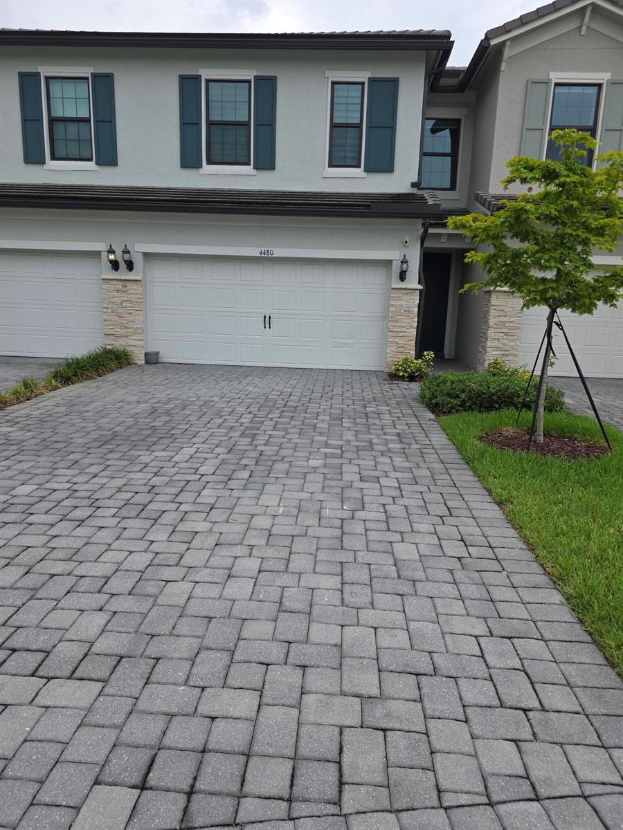 A two-story townhouse exterior features a paved driveway, a white garage door, and stone accents — 4480 W Appleton Cir W, Oakland Park FL 33309, OAKLAND PARK, FL