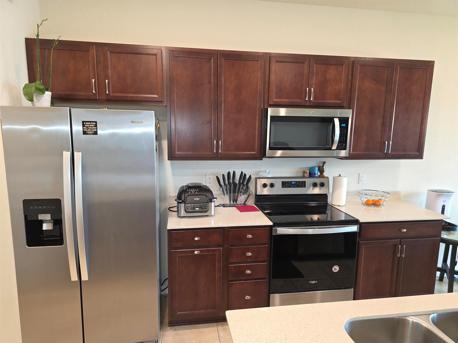 A kitchen features dark wood cabinets, light countertops, a curved island, and three bar stools — 4480 W Appleton Cir W, Oakland Park FL 33309, OAKLAND PARK, FL