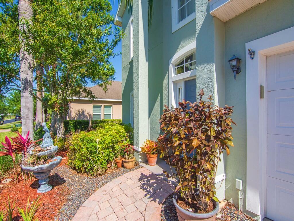 A light green house exterior features a stone walkway, potted plants, and a small fountain — 521 N Valencia Circle SW, Vero Beach FL 32968, VERO BEACH, FL