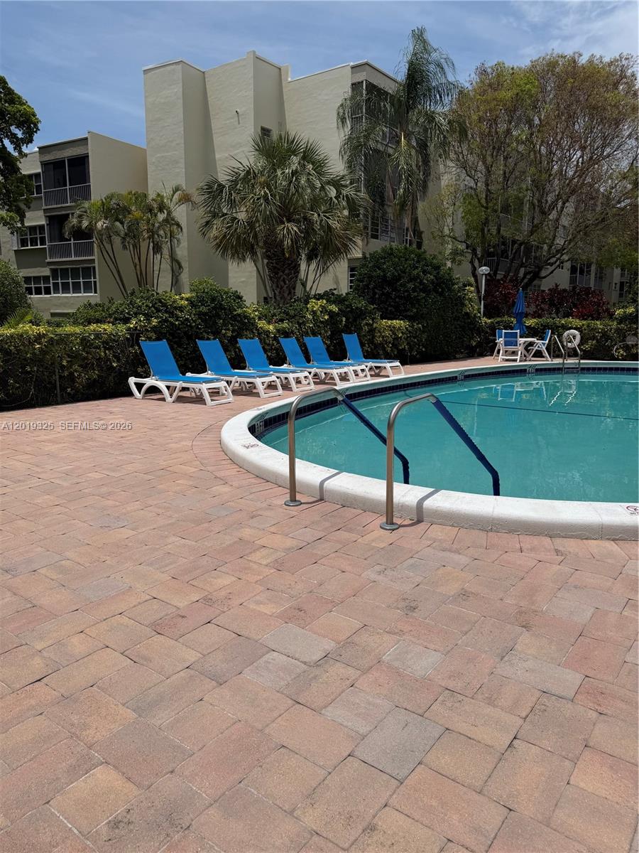 A swimming pool with blue lounge chairs sits on a paved deck by a building — 6701 Cypress Rd # 109, Plantation FL 33317, PLANTATION, FL