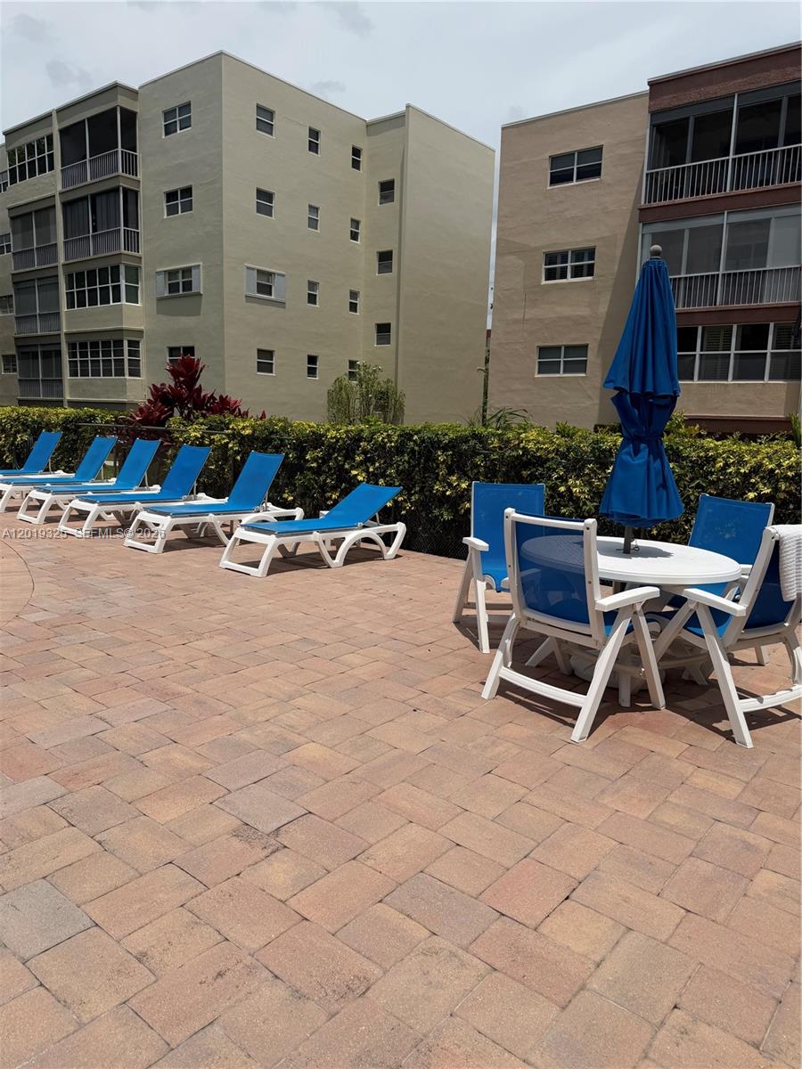 A paved pool deck features lounge chairs, a table with an umbrella, and apartment buildings — 6701 Cypress Rd # 109, Plantation FL 33317, PLANTATION, FL