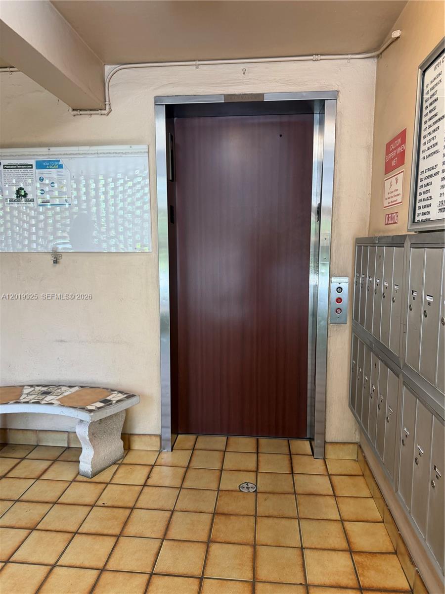 An elevator with wood-look doors is centered in a tiled lobby with mailboxes and seating — 6701 Cypress Rd # 109, Plantation FL 33317, PLANTATION, FL