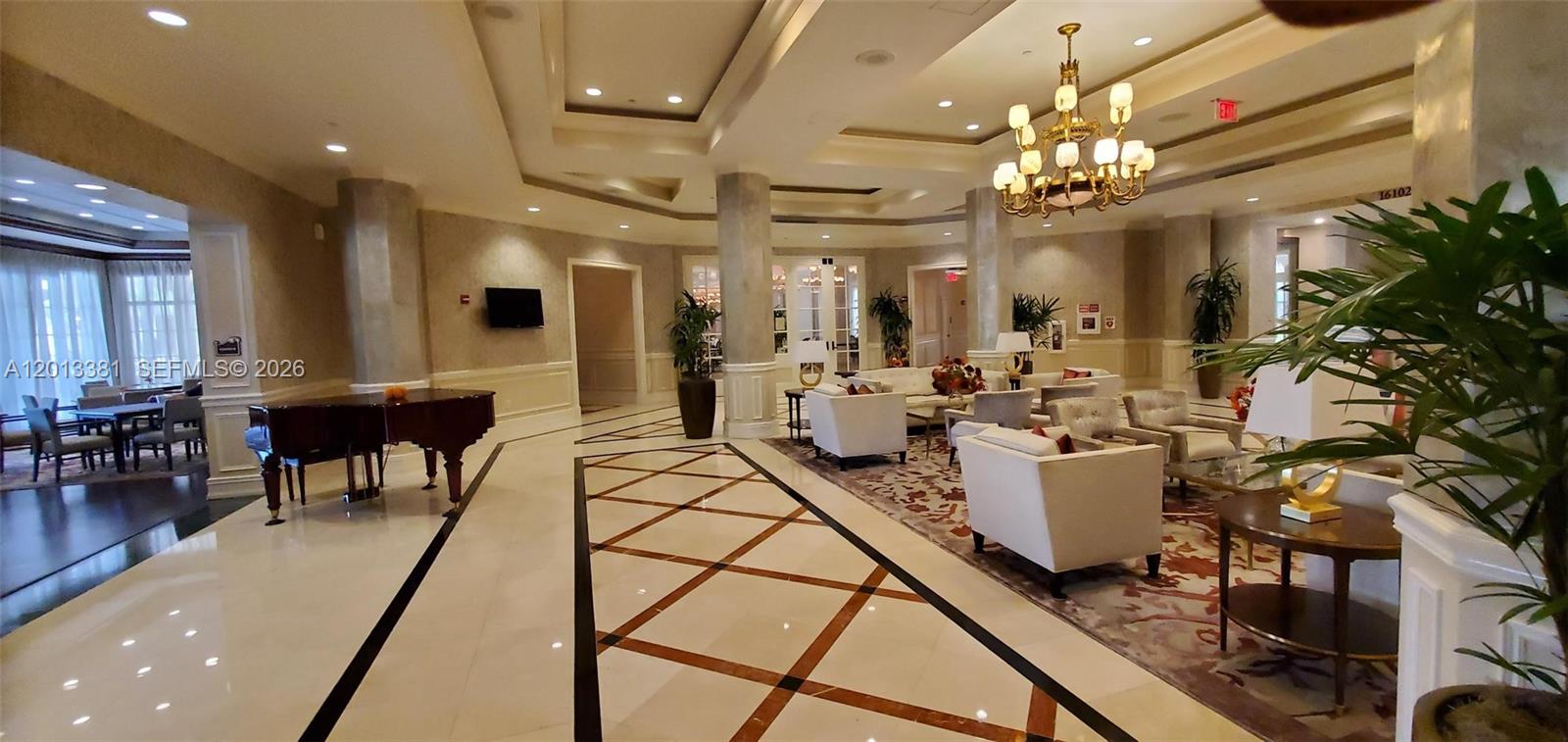 A spacious, well-lit lobby features a grand piano, white seating areas, and decorative tile flooring — 16102 Emerald Estates Dr # 428, Weston FL 33331, WESTON, FL