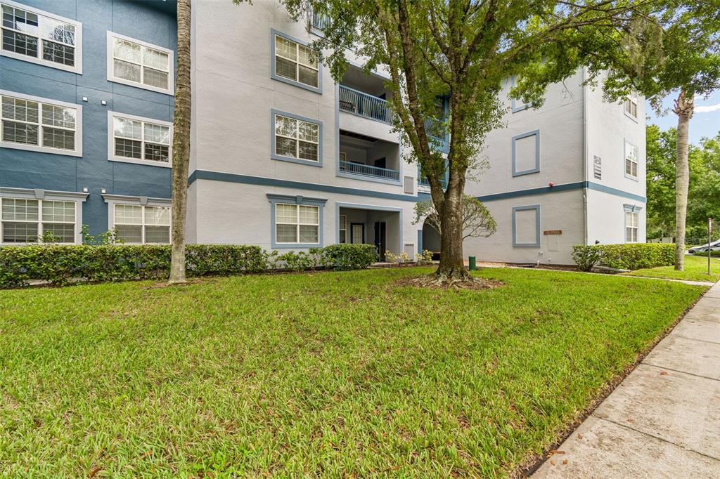 A multi-story apartment building exterior features light-colored stucco walls, blue accents, and a grassy lawn — 1640 VILLA CAPRI CIRCLE UNIT 208, ODESSA, FL
