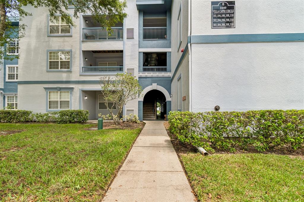 A concrete walkway leads to the arched entrance of a three-story apartment building — 1640 VILLA CAPRI CIRCLE UNIT 208, ODESSA, FL