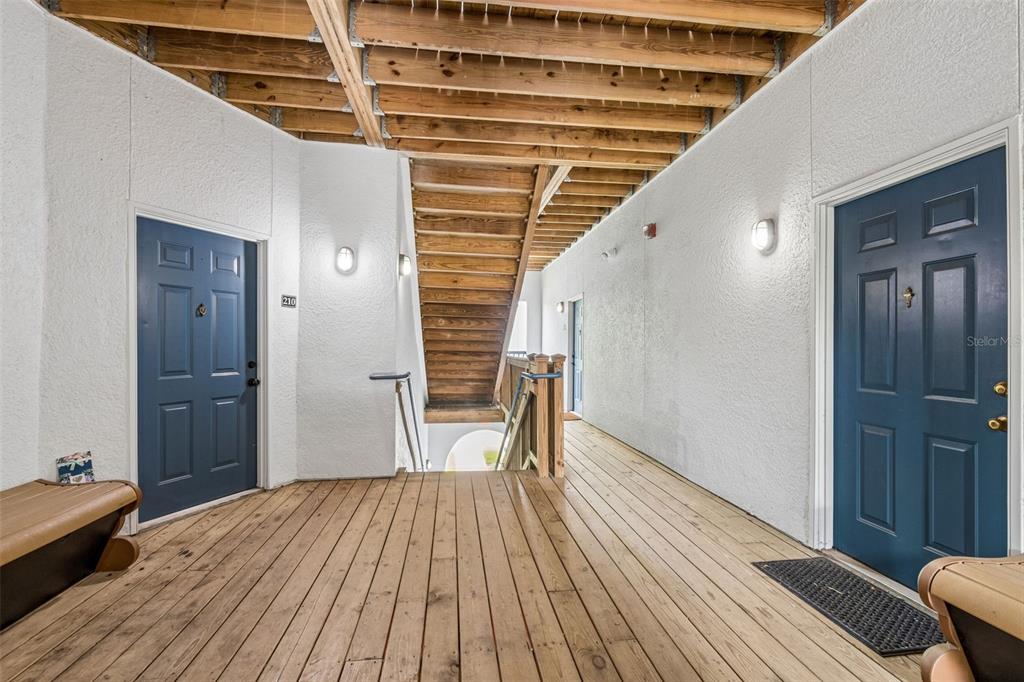 An outdoor wooden walkway leads to two blue doors with a central wooden staircase — 1640 VILLA CAPRI CIRCLE UNIT 208, ODESSA, FL