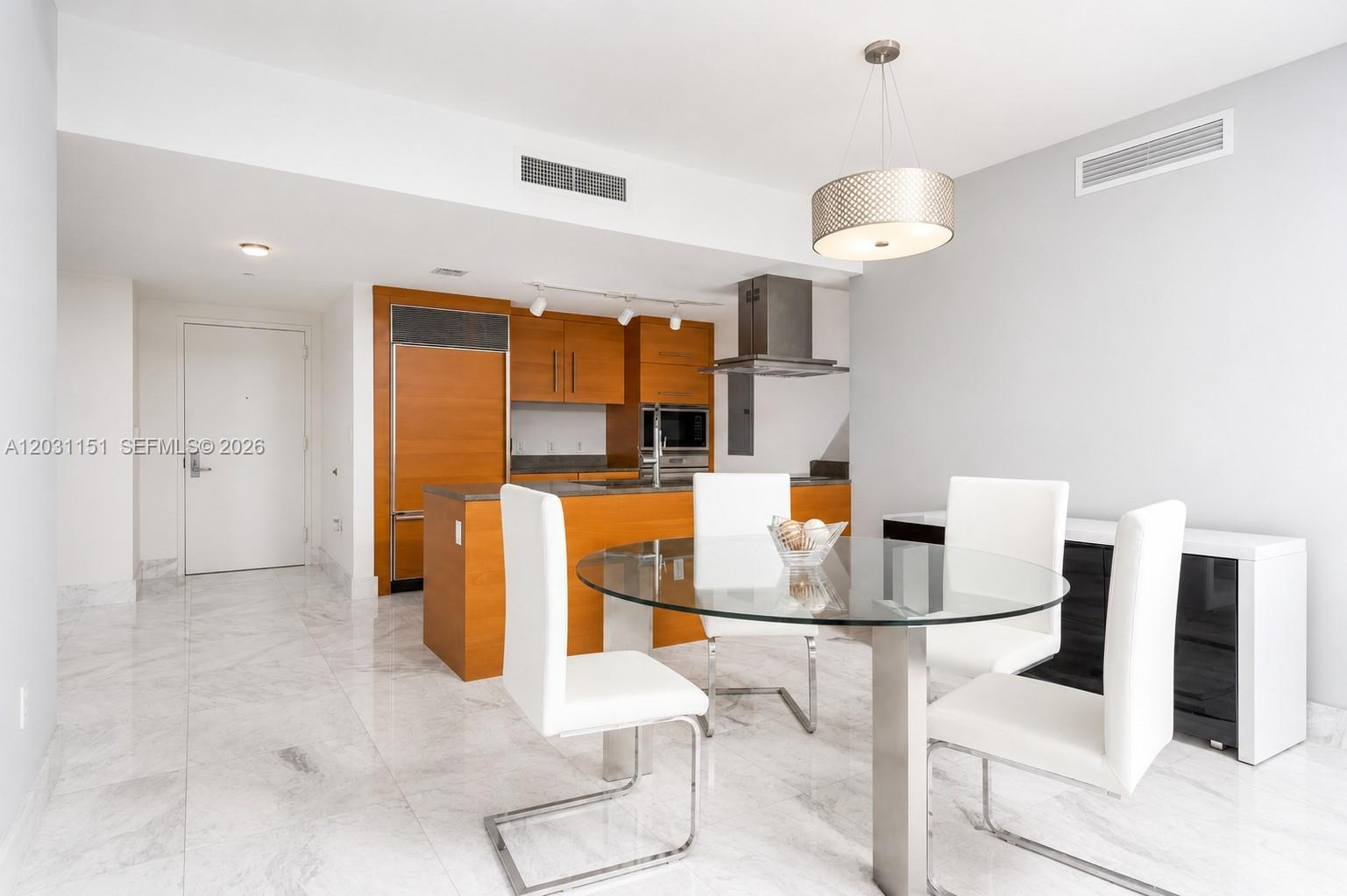 A dining area with a glass table and white chairs sits before an open kitchen — 495 Brickell Ave # 705, Miami FL 33131, MIAMI, FL