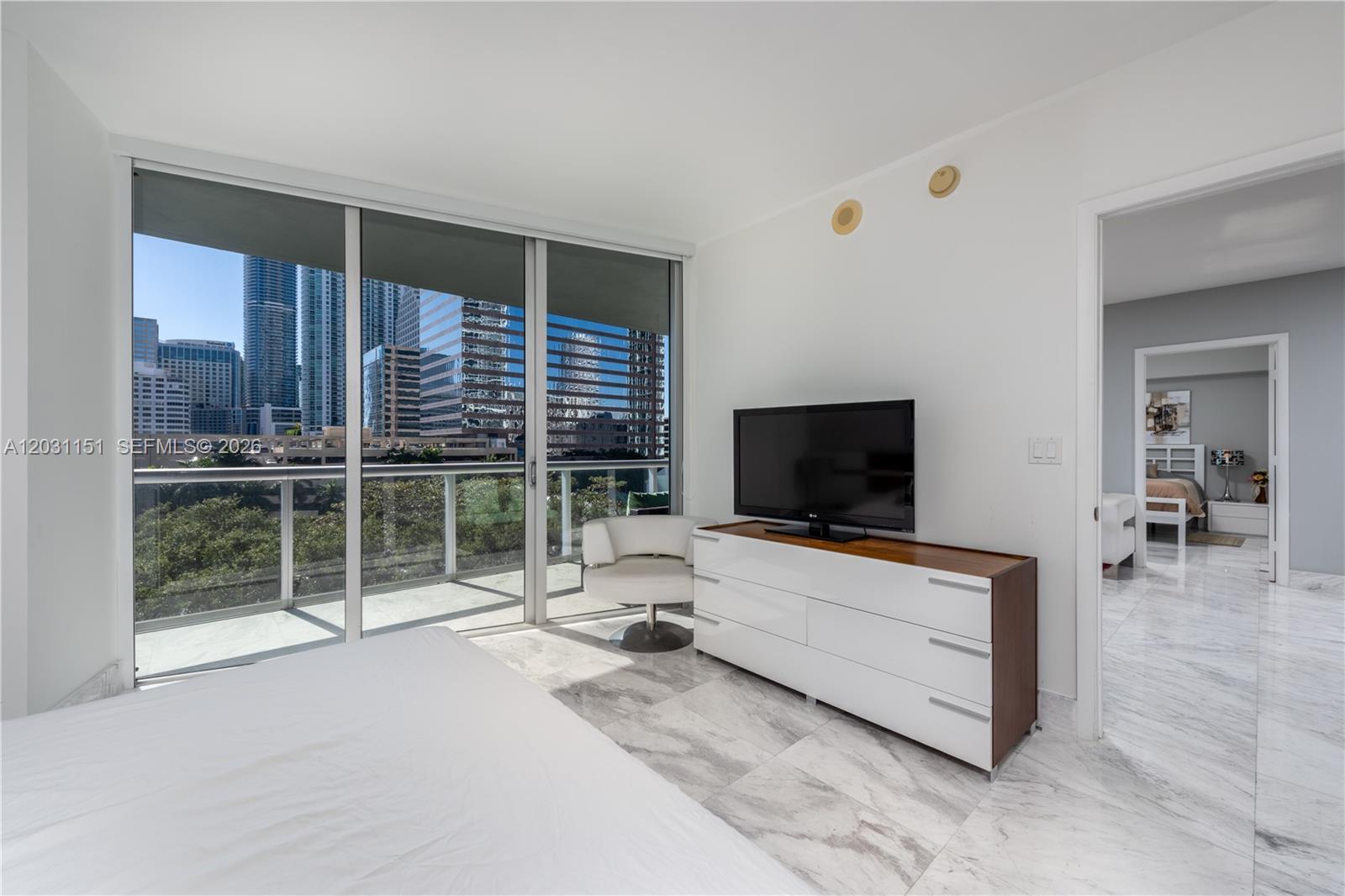 A bedroom with marble floors, a dresser with a television, and a balcony overlooking city buildings — 495 Brickell Ave # 705, Miami FL 33131, MIAMI, FL
