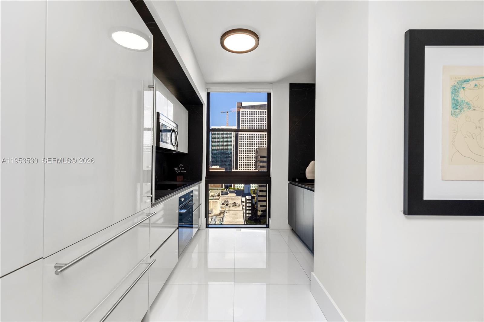 A modern galley kitchen features white glossy cabinets, dark stone accents, and a city view — 1010 Brickell Ave # 1701, Miami FL 33131, MIAMI, FL