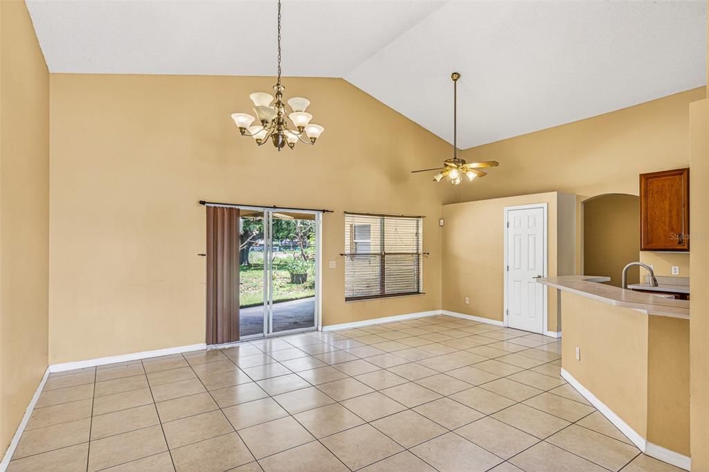 A living and dining area with vaulted ceilings, tile floors, a ceiling fan, and sliding doors — 1000 ROYAL MARQUIS CIRCLE, OCOEE, FL