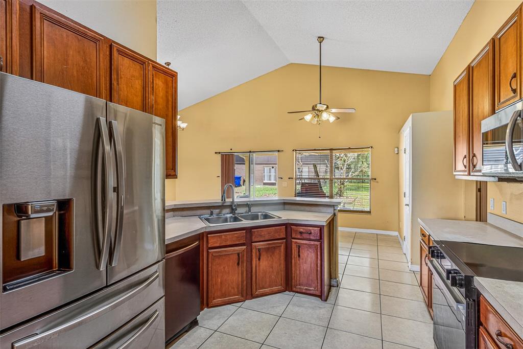 A kitchen with wood cabinets, stainless steel appliances, tile flooring, and a vaulted ceiling — 1000 ROYAL MARQUIS CIRCLE, OCOEE, FL