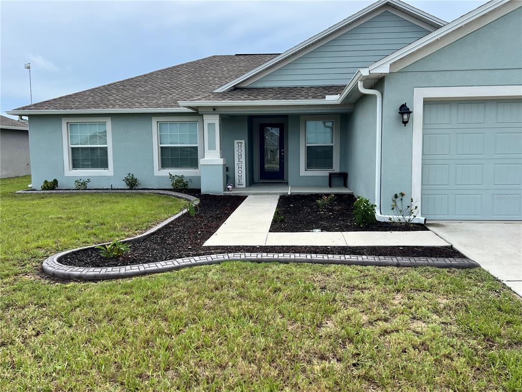 The exterior of a light blue house features a concrete walkway, mulch beds, and a garage — 513 CENTRAL RIDGE LANE, FROSTPROOF, FL
