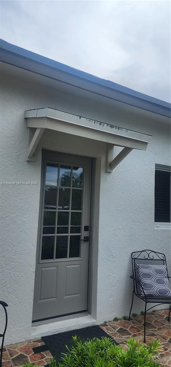 A gray door with a glass grid sits under a small wooden awning on a stucco wall — 12641 SW 210th Ter # A, Miami FL 33177, MIAMI, FL