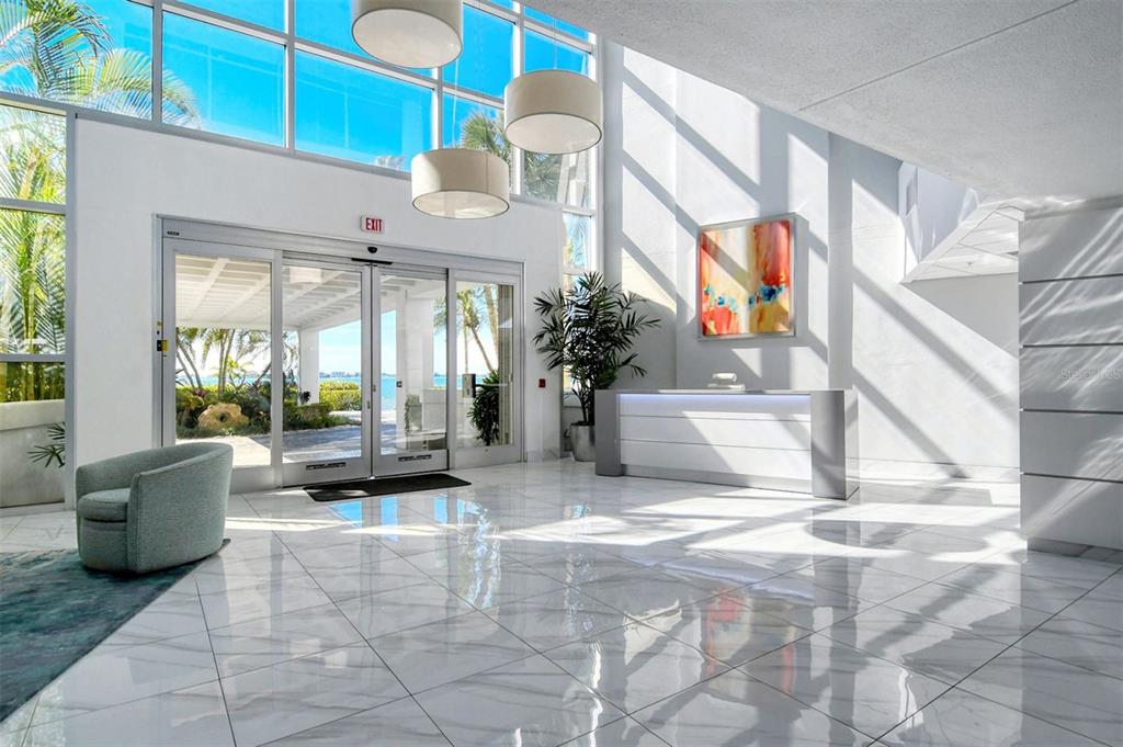 A bright lobby features white marble floors, a reception desk, and floor-to-ceiling windows — 888 BOULEVARD OF THE ARTS UNIT 505, SARASOTA, FL