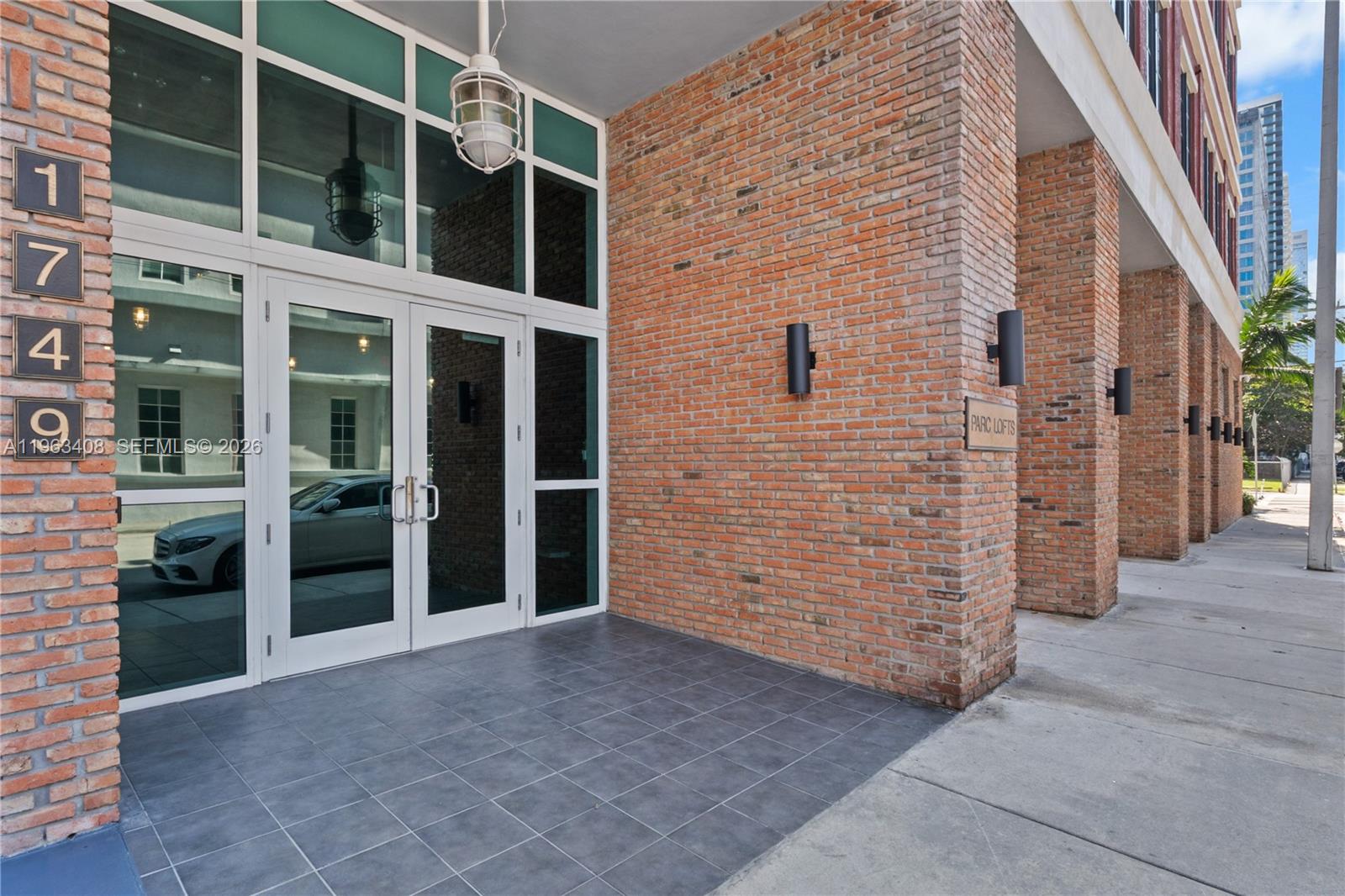 The exterior entrance of a brick building features glass double doors and modern wall sconces — 1749 NE Miami Ct # 605, Miami FL 33132, MIAMI, FL