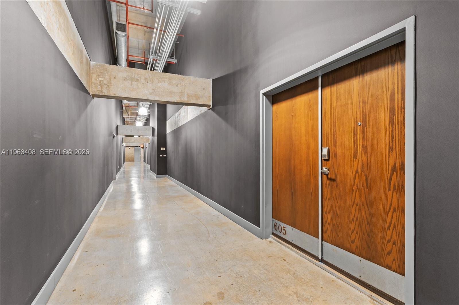 A long hallway with dark walls, exposed industrial ceiling pipes, and a wooden double door — 1749 NE Miami Ct # 605, Miami FL 33132, MIAMI, FL