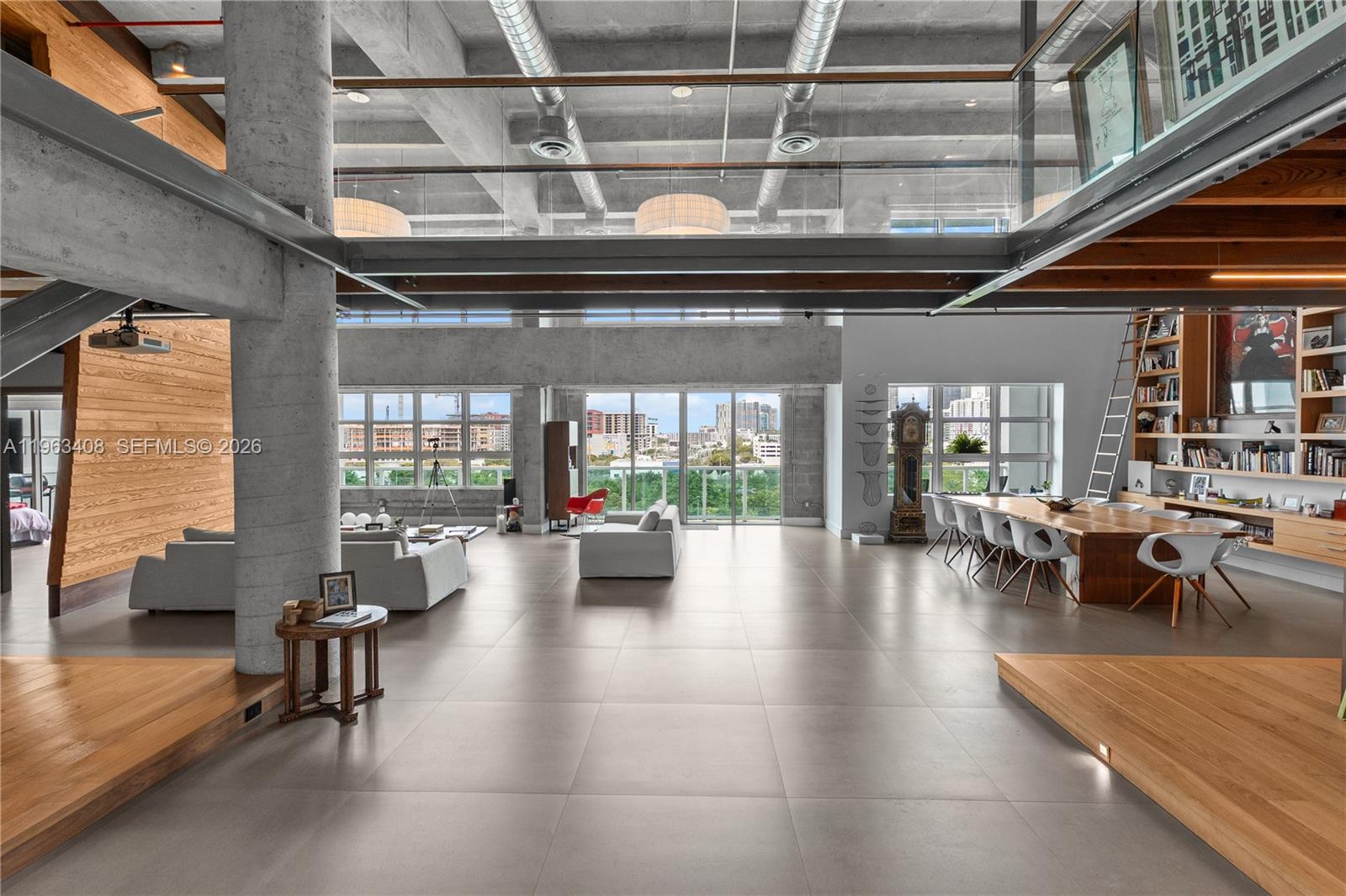 A spacious, open-concept loft features concrete ceilings, large windows, and a mix of tile and wood flooring — 1749 NE Miami Ct # 605, Miami FL 33132, MIAMI, FL