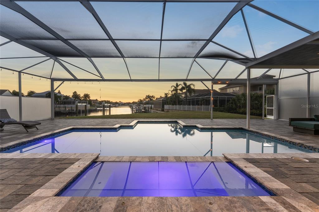 A screened-in pool and spa area overlooks a canal at sunset — 5603 TYBEE ISLAND DRIVE, APOLLO BEACH, FL
