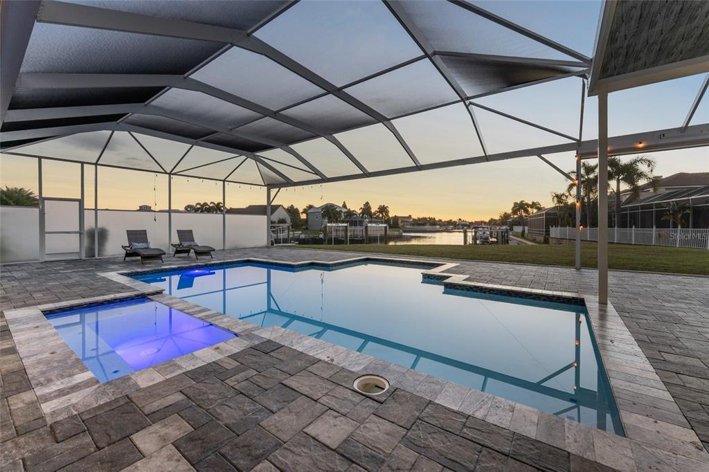 A screened-in pool and spa area with stone pavers overlooks a canal at sunset — 5603 TYBEE ISLAND DRIVE, APOLLO BEACH, FL