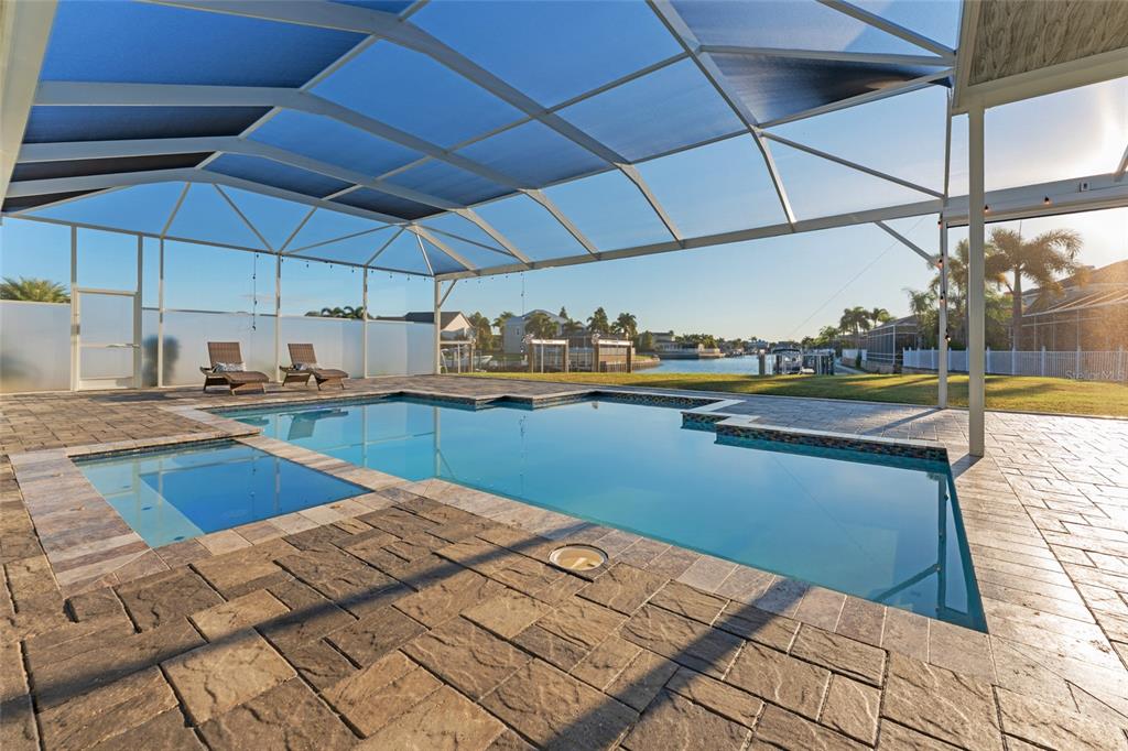 A screened-in pool and spa area with stone pavers overlooking a canal and backyard — 5603 TYBEE ISLAND DRIVE, APOLLO BEACH, FL