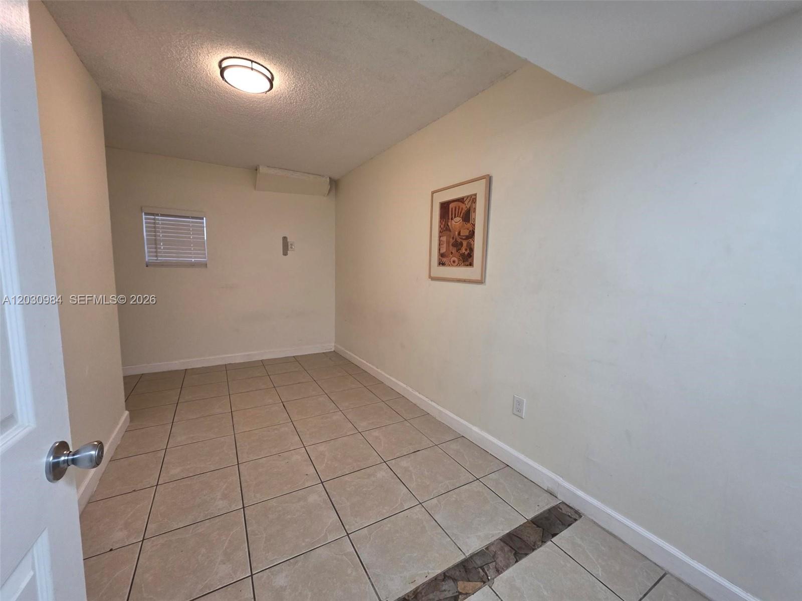 An empty room features beige tile flooring, a small window, and a wall-mounted picture — 8550 SW 109th Ave # 228, Miami FL 33173, MIAMI, FL