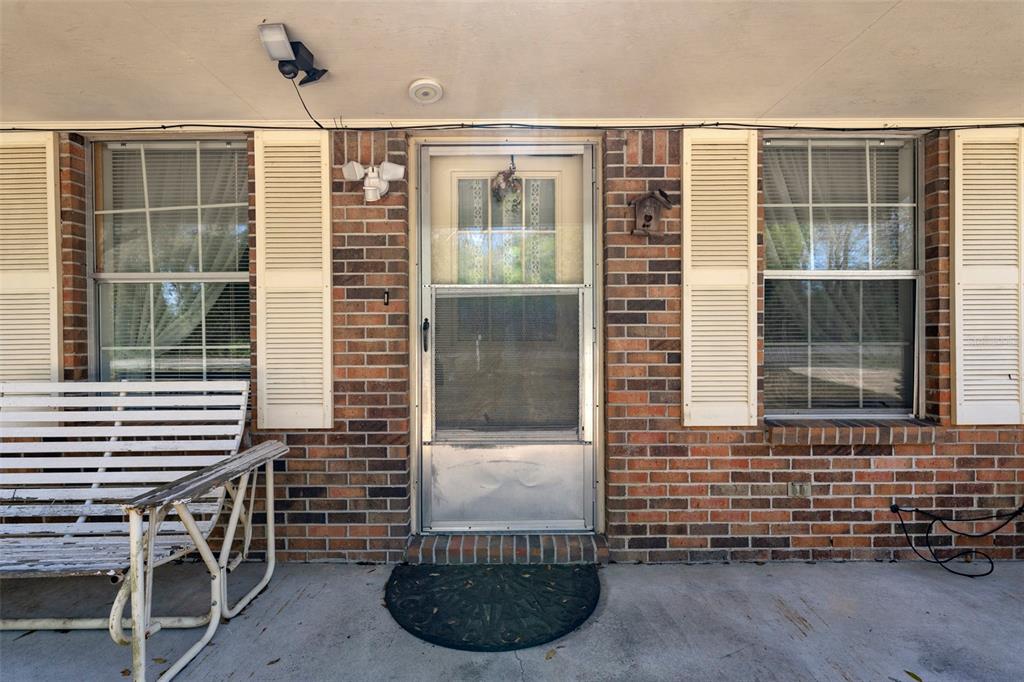 A brick house exterior features a front porch with a white bench and storm door — 1788 HIGHWAY 10A, PONCE DE LEON, FL