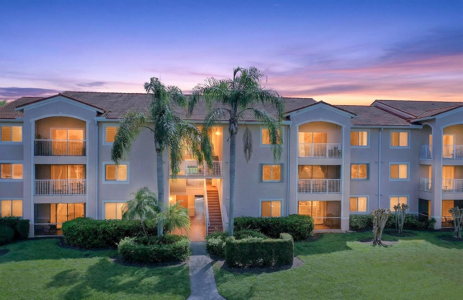 A three-story apartment building with balconies and palm trees at sunset — 1640 N 42nd Circle Unit 305, Vero Beach FL 32967, VERO BEACH, FL
