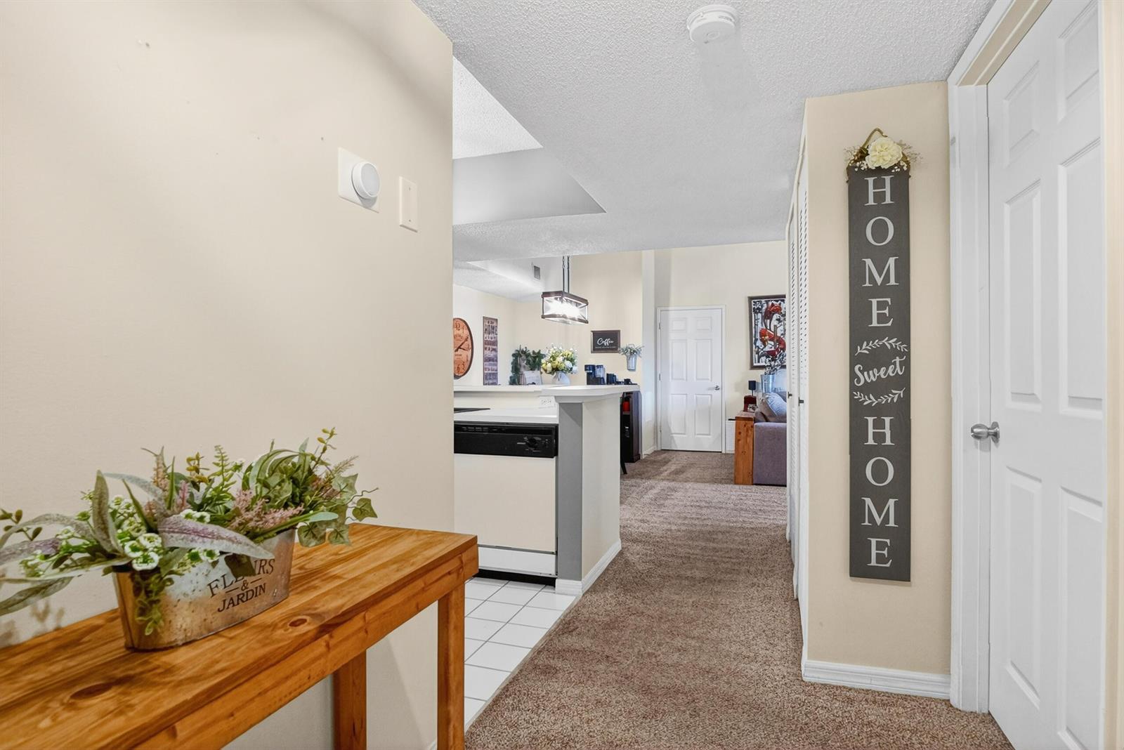 A hallway with carpeted flooring leads to a kitchen with white tile and appliances — 1640 N 42nd Circle Unit 305, Vero Beach FL 32967, VERO BEACH, FL