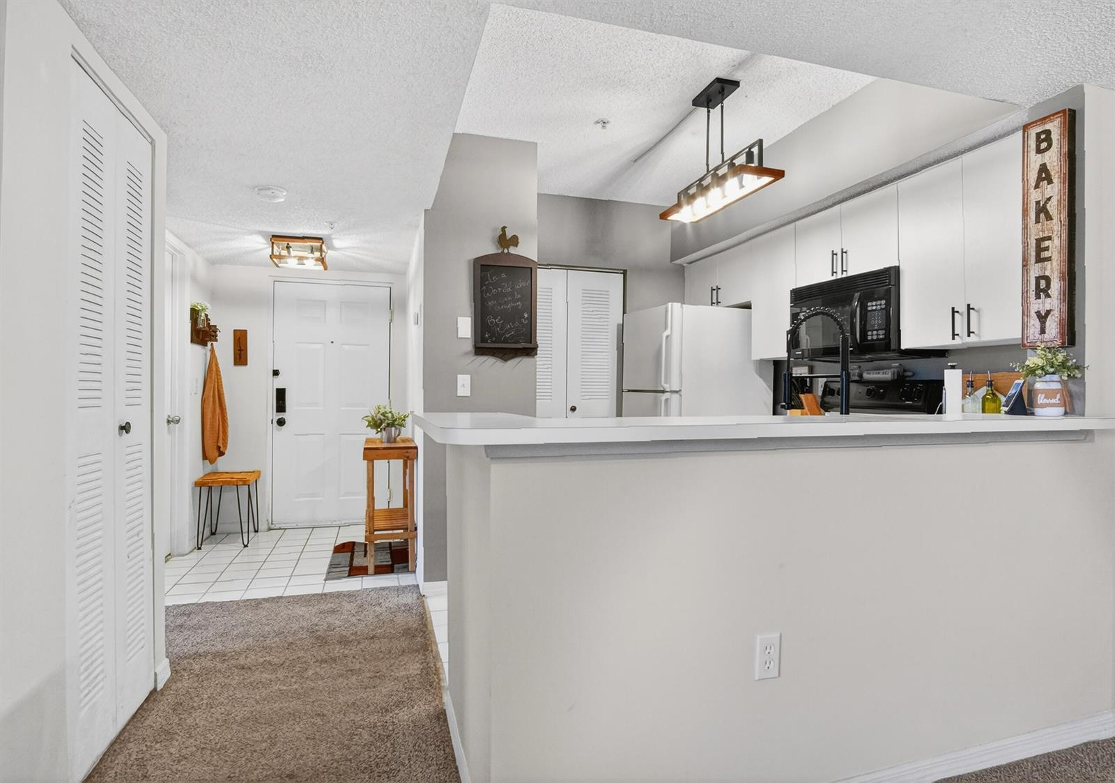 A kitchen with white cabinets and a breakfast bar overlooks an entryway with tiled floors — 1640 N 42nd Circle Unit 305, Vero Beach FL 32967, VERO BEACH, FL