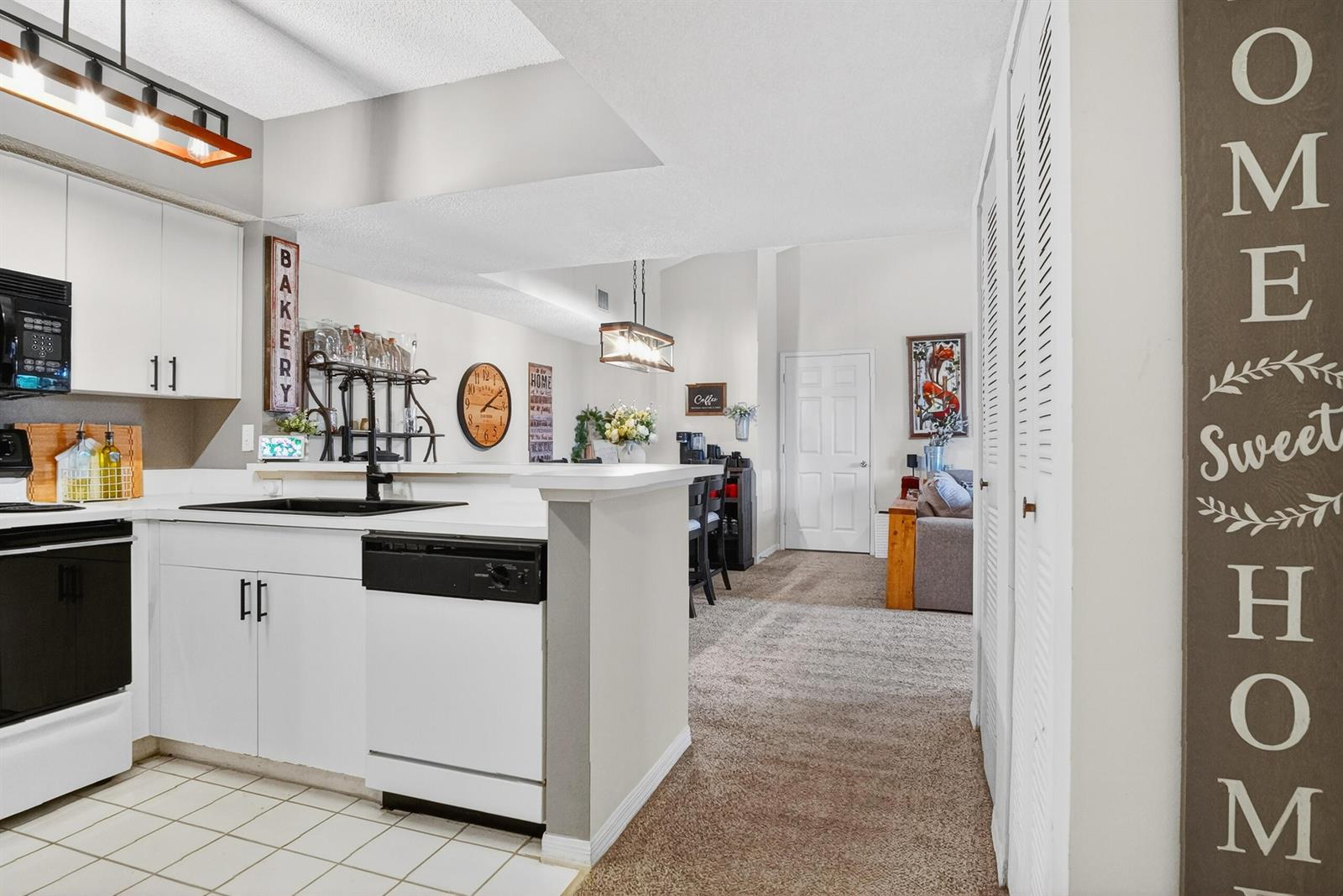 A kitchen with white cabinets and a dishwasher opens into a carpeted living area — 1640 N 42nd Circle Unit 305, Vero Beach FL 32967, VERO BEACH, FL