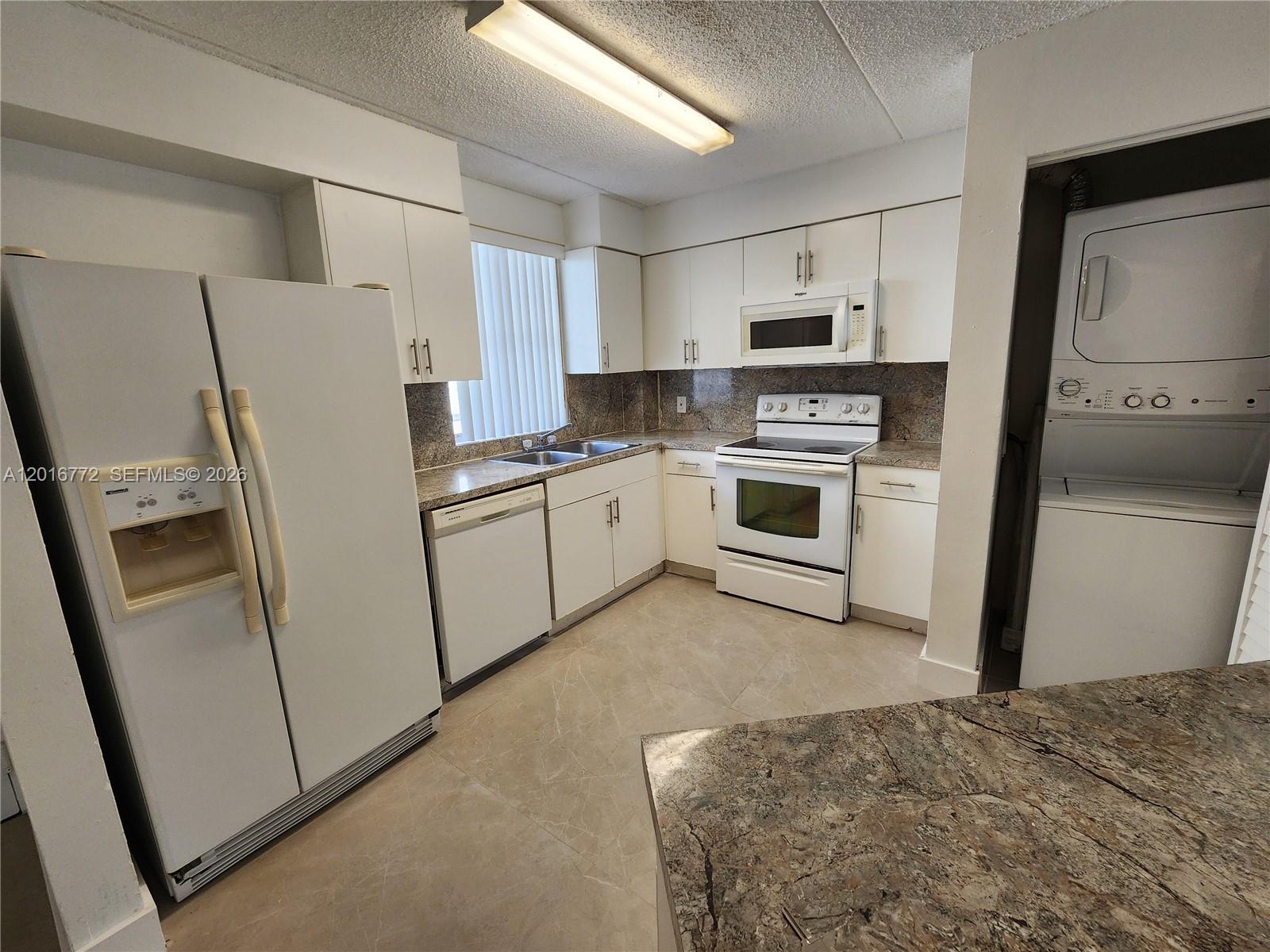 A kitchen features white cabinetry, granite countertops, white appliances, and a stacked laundry unit — 6065 NW 186th St # 208, Hialeah FL 33015, HIALEAH, FL