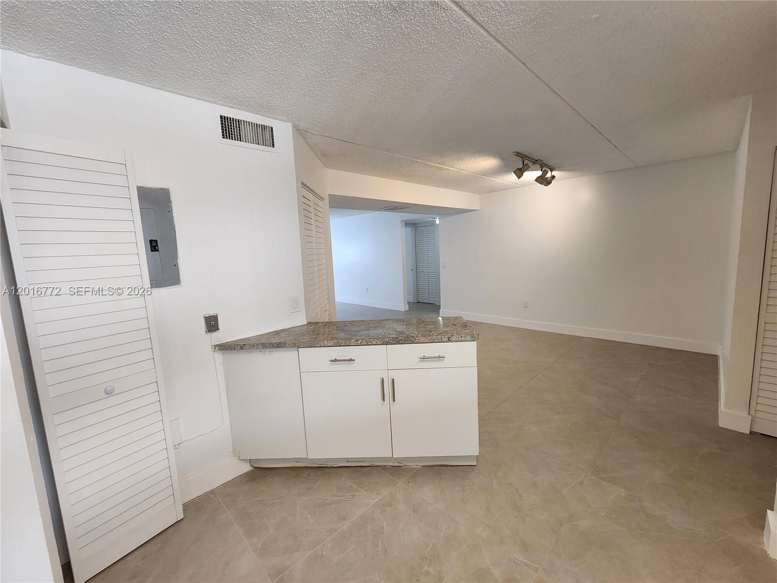 A kitchen area features white cabinets, a granite countertop, and light-colored tile flooring — 6065 NW 186th St # 208, Hialeah FL 33015, HIALEAH, FL