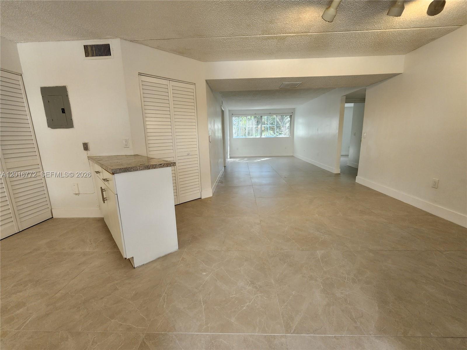An open-concept living area features light-colored tile flooring, white walls, and a small kitchen counter — 6065 NW 186th St # 208, Hialeah FL 33015, HIALEAH, FL