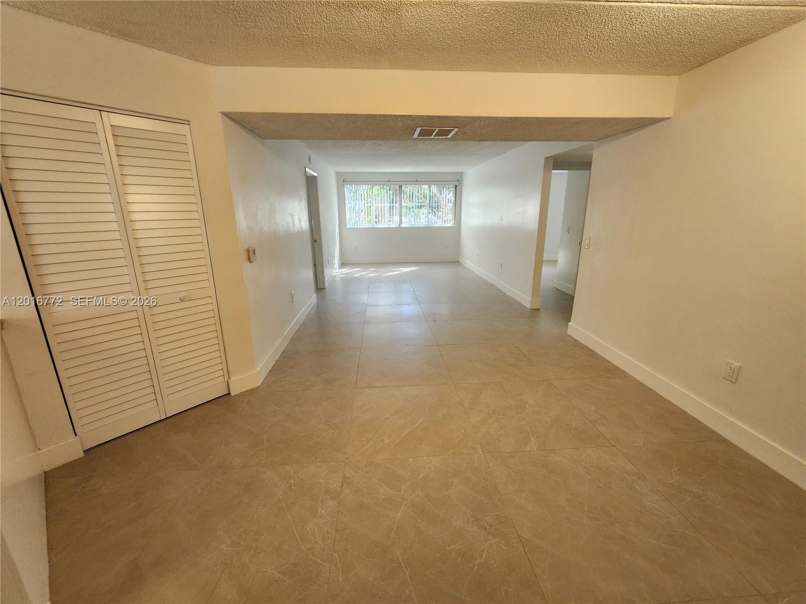 A long, empty room features light-colored tile flooring, white walls, and a louvered closet door — 6065 NW 186th St # 208, Hialeah FL 33015, HIALEAH, FL