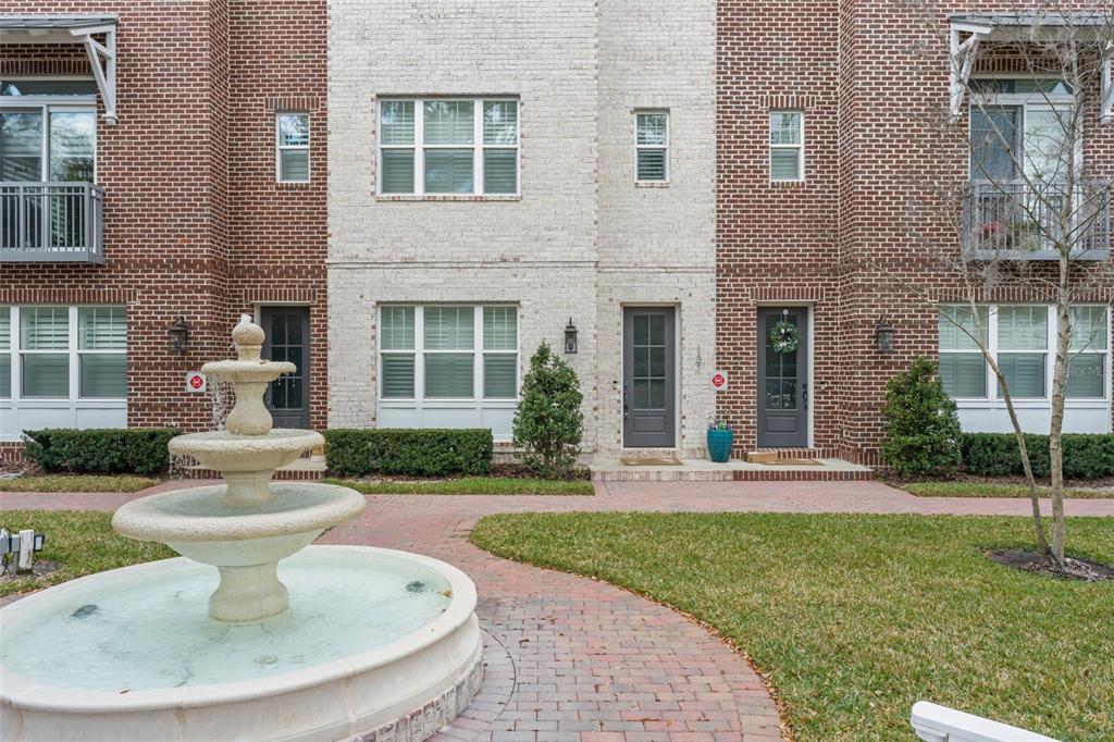 A tiered stone fountain sits in front of a brick townhome with multiple entryways — 131 OAK LAUREL DRIVE, WINTER GARDEN, FL