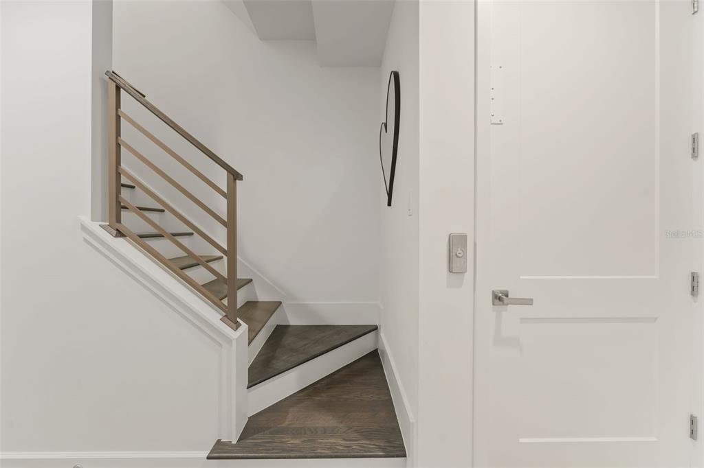 A staircase with dark wood treads and a metal railing sits beside a white door — 131 OAK LAUREL DRIVE, WINTER GARDEN, FL