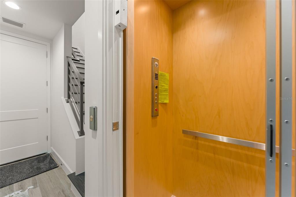 An elevator with light wood paneling stands next to a white door and staircase — 131 OAK LAUREL DRIVE, WINTER GARDEN, FL