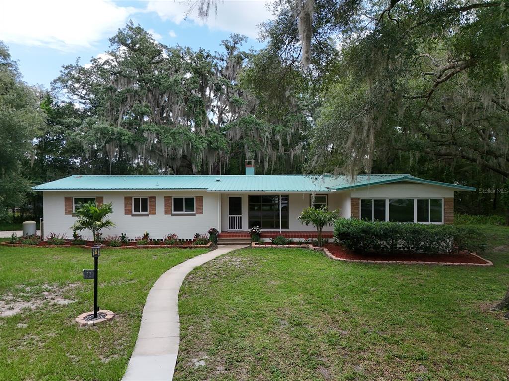 A single-story house with a teal metal roof and white brick exterior sits on a lawn — 22 POINSETTIA DRIVE, DELAND, FL