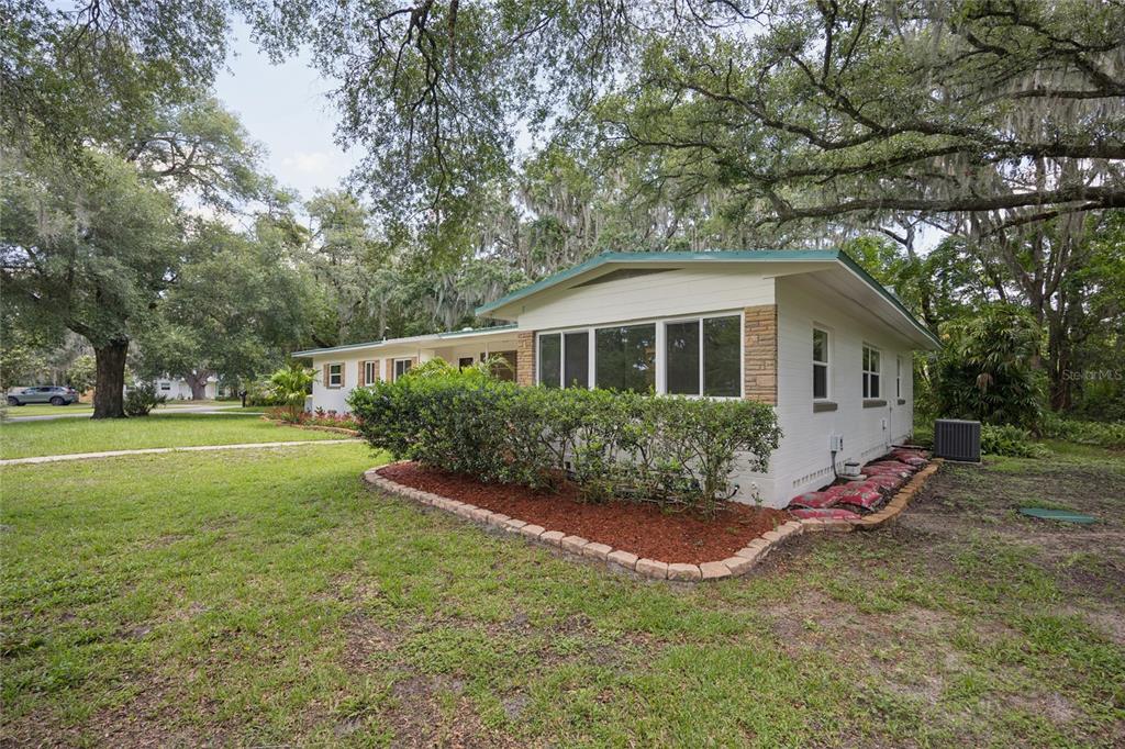 A single-story white house with a stone accent wall sits on a grassy, tree-shaded lot — 22 POINSETTIA DRIVE, DELAND, FL