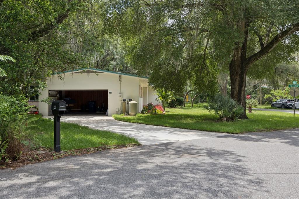 A white house with an open garage sits on a grassy lot under large trees — 22 POINSETTIA DRIVE, DELAND, FL