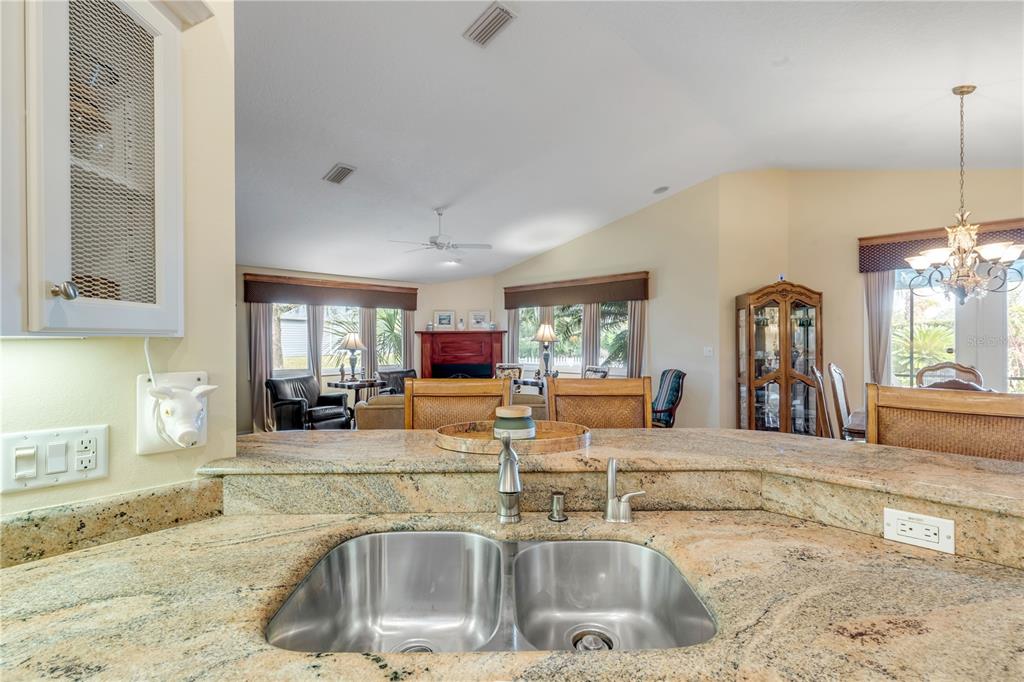 A kitchen sink with granite countertops overlooks a living room with a fireplace — 1098 RED MAPLE WAY, NEW SMYRNA BEACH, FL