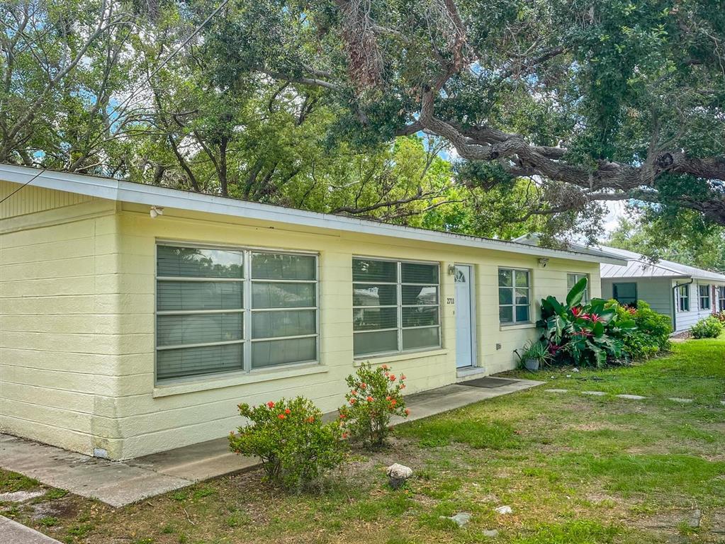 A single-story yellow house with large windows and a front door sits under mature trees — 2711 LYNNHURST STREET, SARASOTA, FL