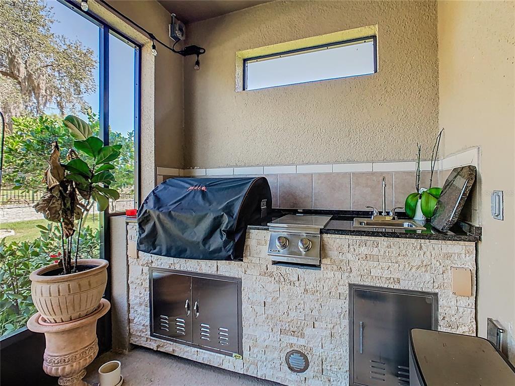 An outdoor kitchen features a covered grill, a small sink, and stone veneer cabinetry — 1731 GOBLET COVE STREET, KISSIMMEE, FL