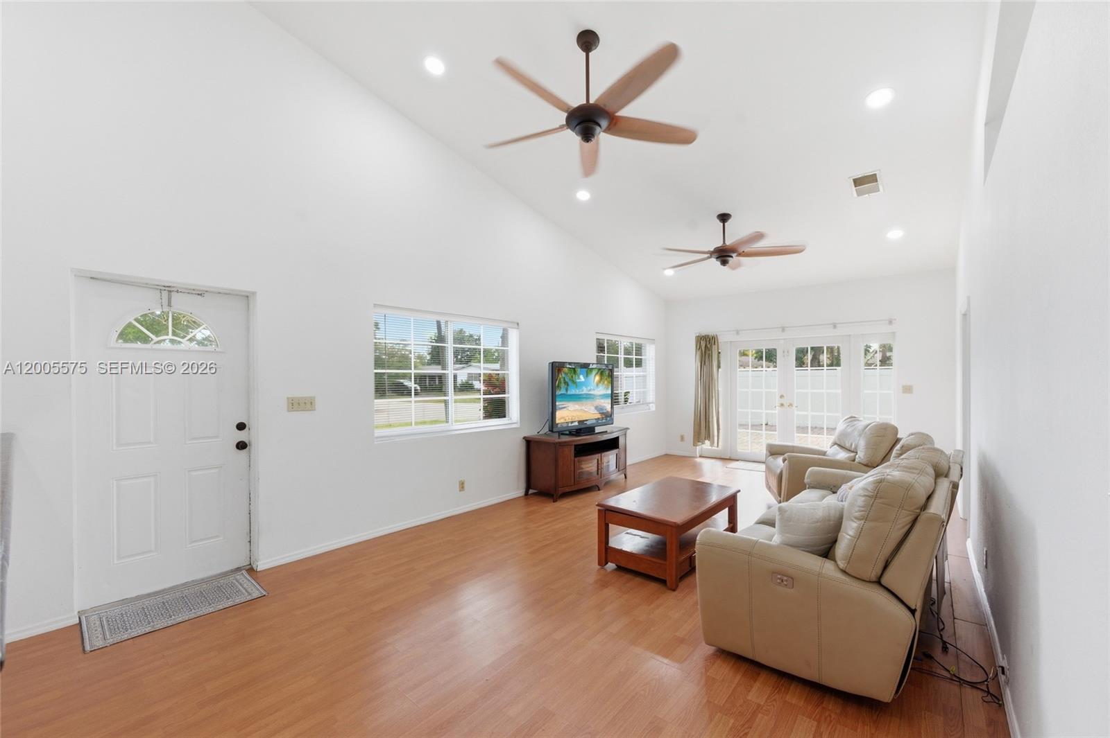 A living room features vaulted ceilings, two ceiling fans, light wood flooring, and beige furniture — 4361 NE 13th Ter, Oakland Park FL 33334, OAKLAND PARK, FL